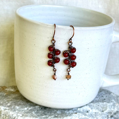 Pair of red beaded earrings hanging over a white mug.
