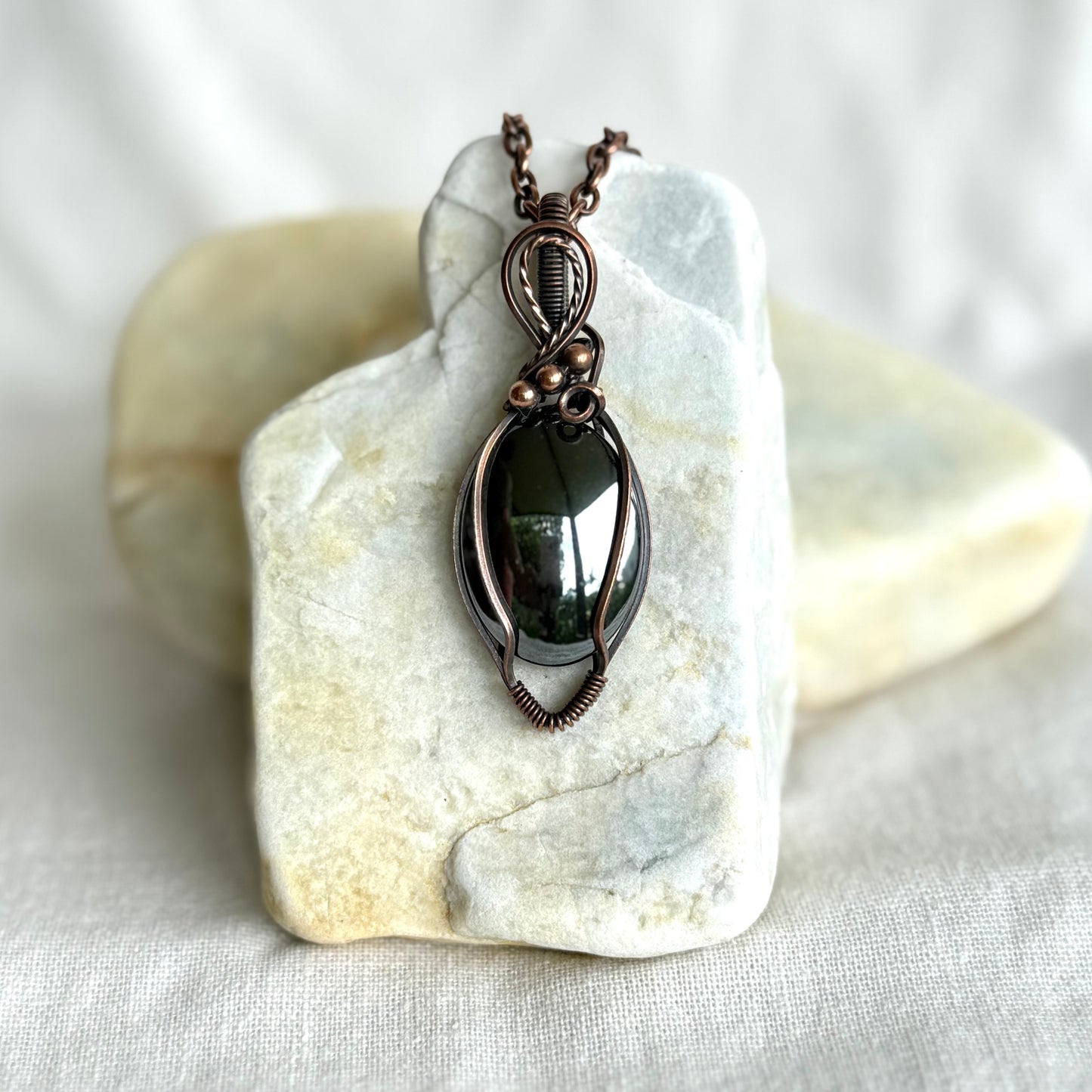 Copper pendant with a hematite stone on a piece of stone on linen background