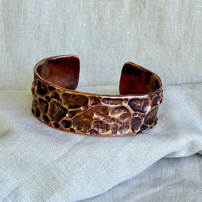 Copper cuff bracelet with textured surface on a light fabric background