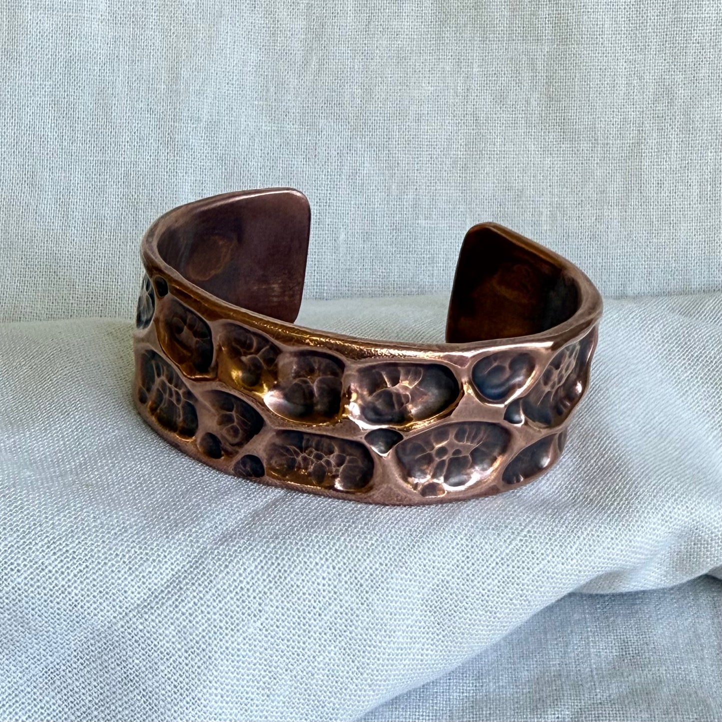 Copper cuff with textured surface on a light fabric background