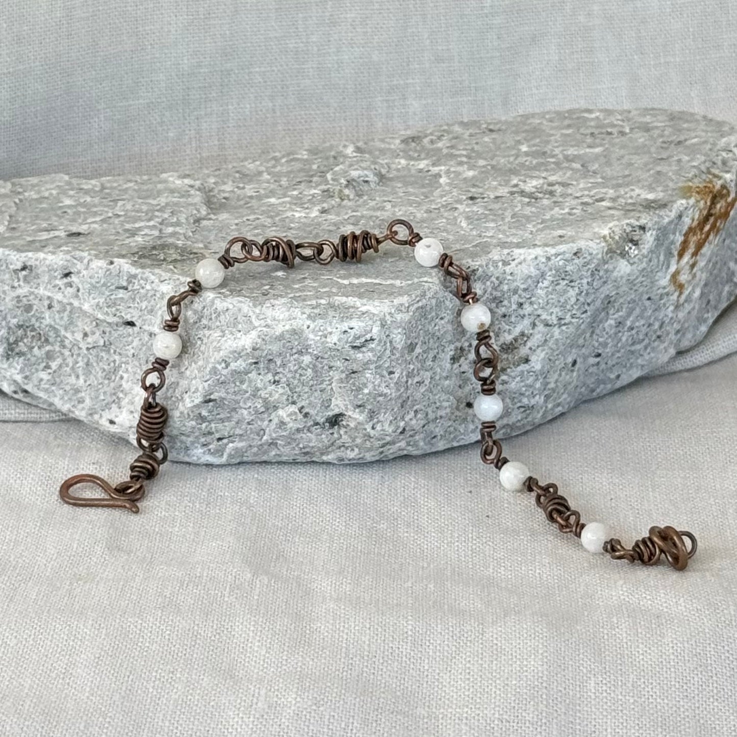Copper Bracelet with small white moonstones on a stone surface with linen background