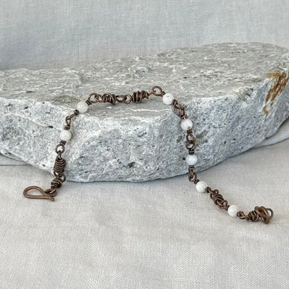 Copper Bracelet with small white moonstones on a stone surface with linen background