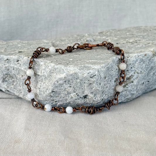 Copper Bracelet with small white moonstones on a stone surface with linen background