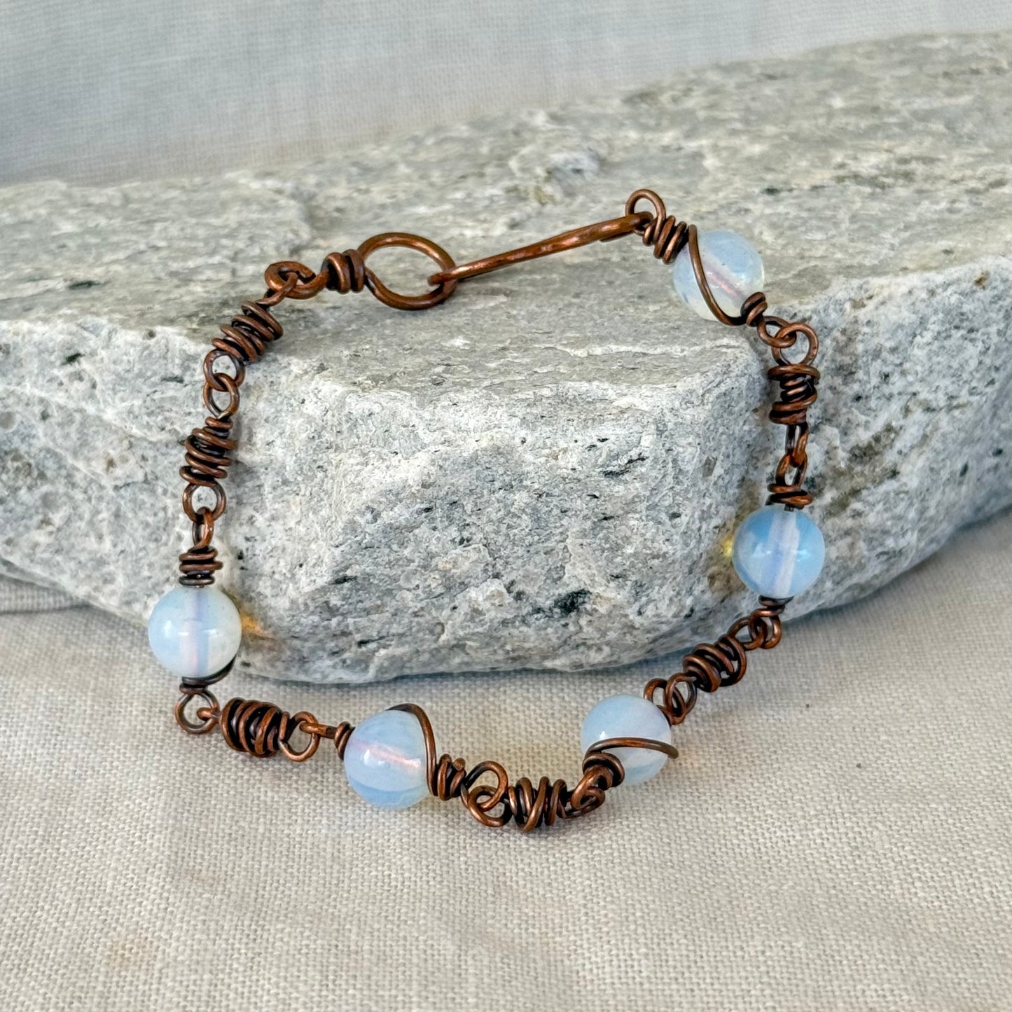 Copper Bracelet with opalite beads and on a stone surface with linen background