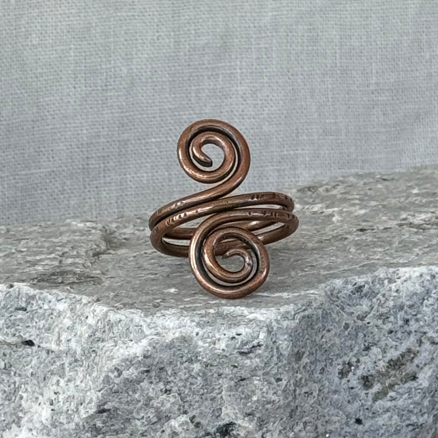 Copper spiral ring on a textured stone surface with a linen background