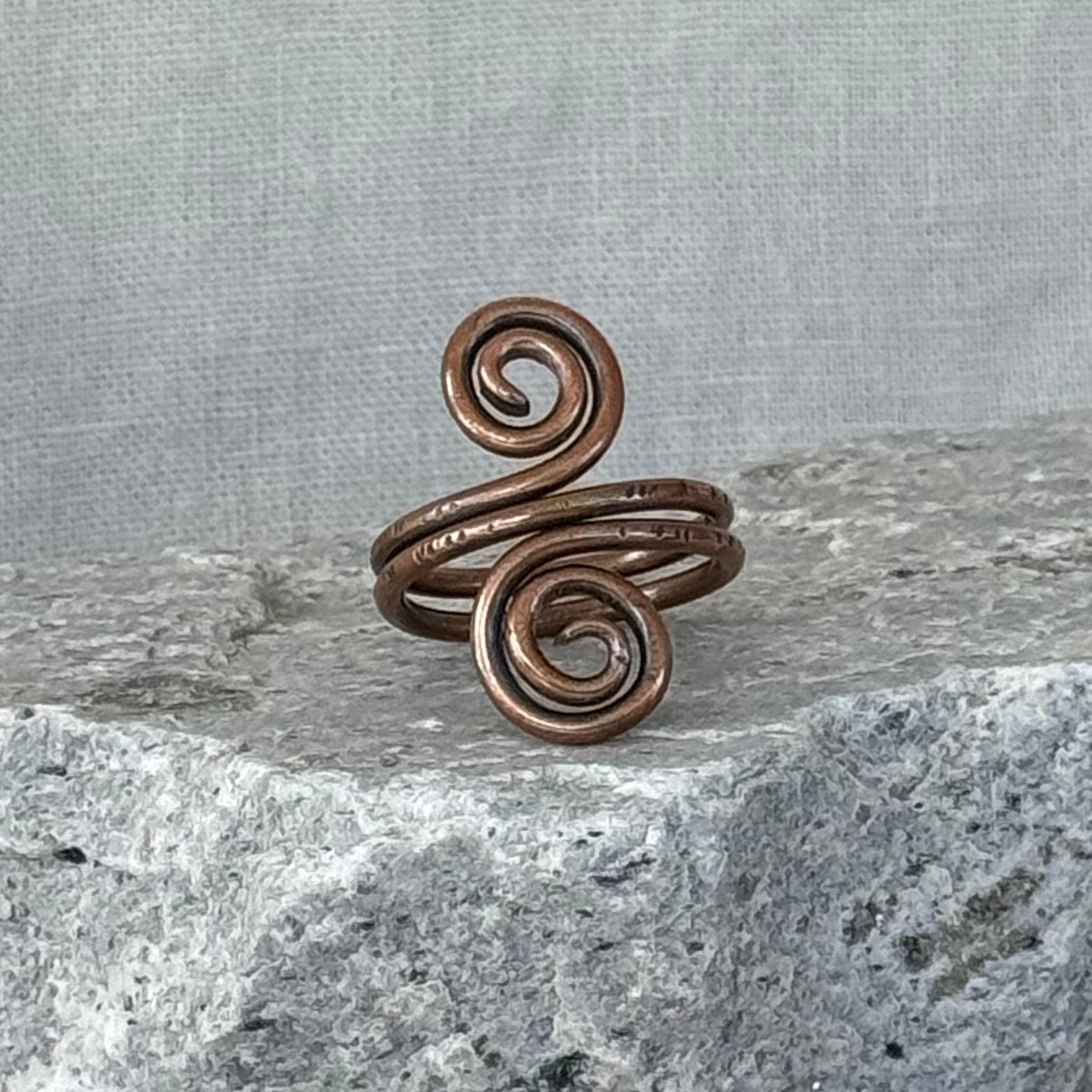 Copper spiral ring on a textured stone surface with a linen background