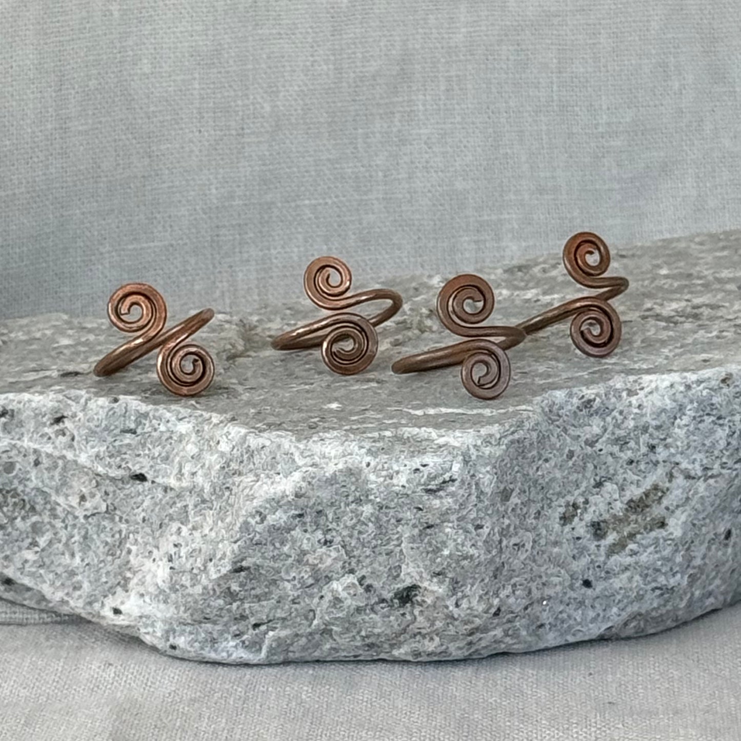 Set of four copper spiral toe rings on a stone surface with a linen fabric background