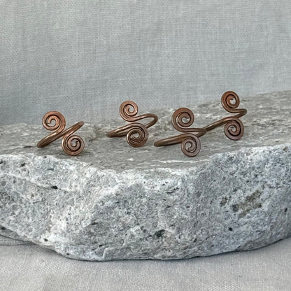 Set of four copper spiral toe rings on a stone surface with a linen fabric background