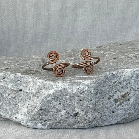 Pair of copper spiral toe rings on a stone surface with a linen background