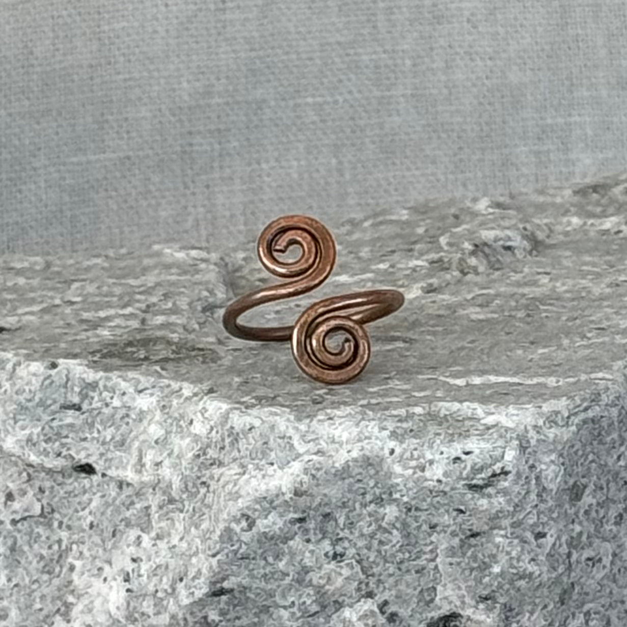 Copper spiral toe ring on a textured stone surface with a linen background