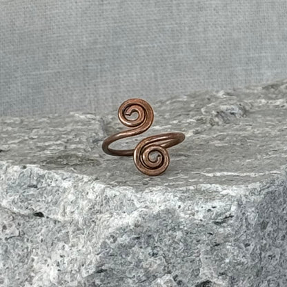 Copper spiral toe ring on a textured stone surface with a linen background