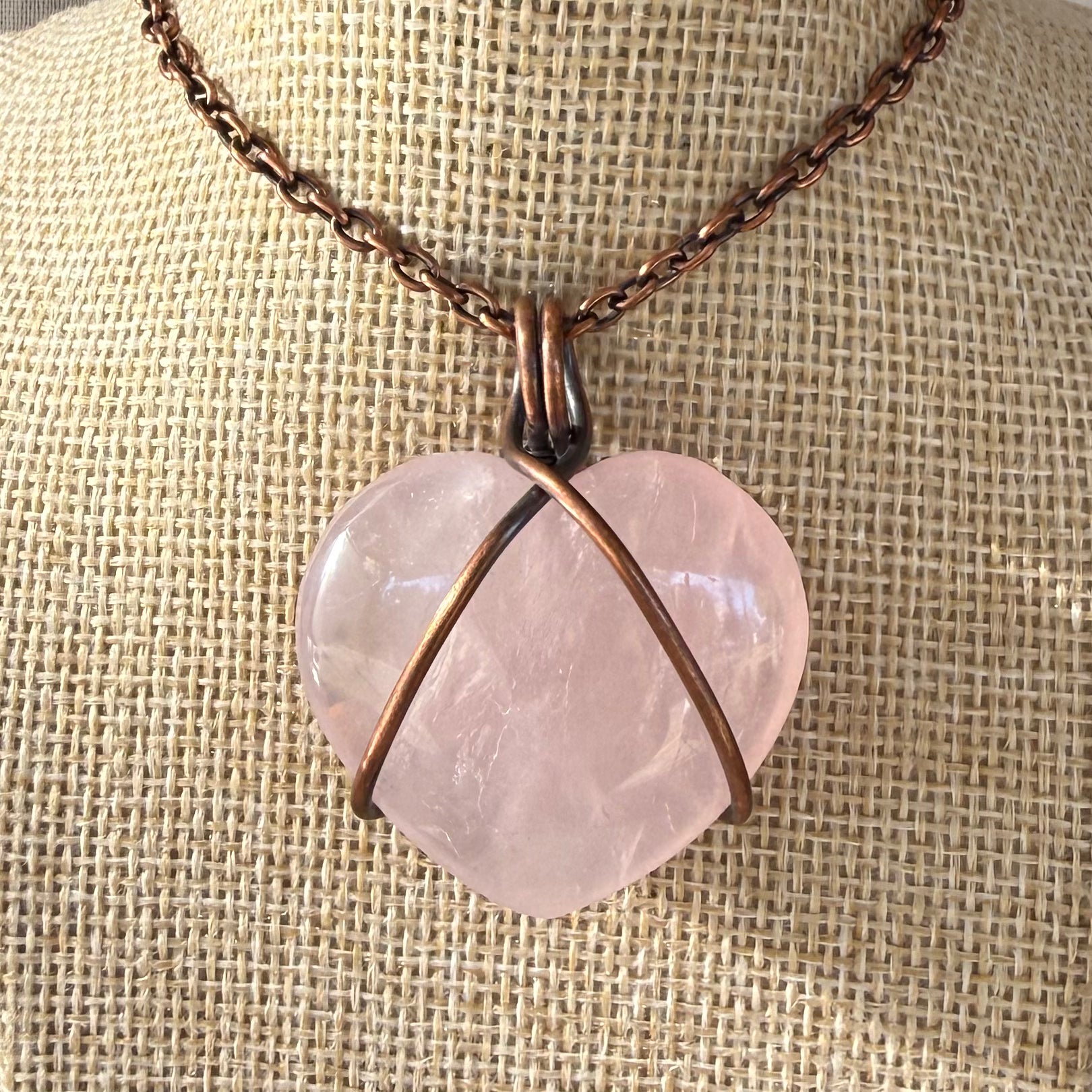Necklace with a heart-shaped pink stone pendant on a textured beige background