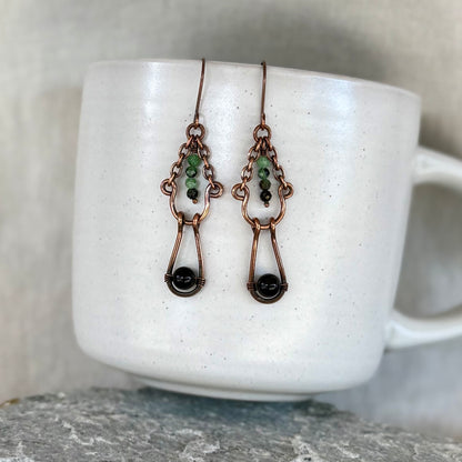 Copper earrings with green and black beads on a white mug with linen background