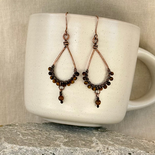 copper teardrop earrings with beads on a mug against a linen background