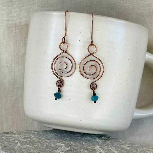 Pair of spiral earrings with blue beads on a white mug.