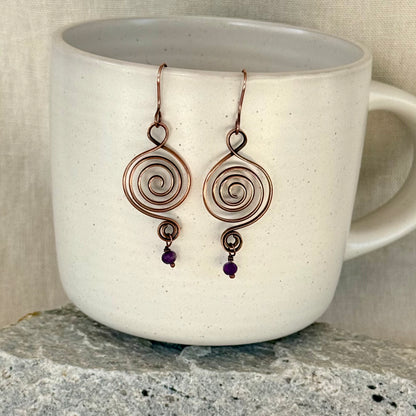 Pair of spiral earrings with purple beads on a white mug.