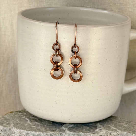 Copper chain earrings on a white mug with a neutral background