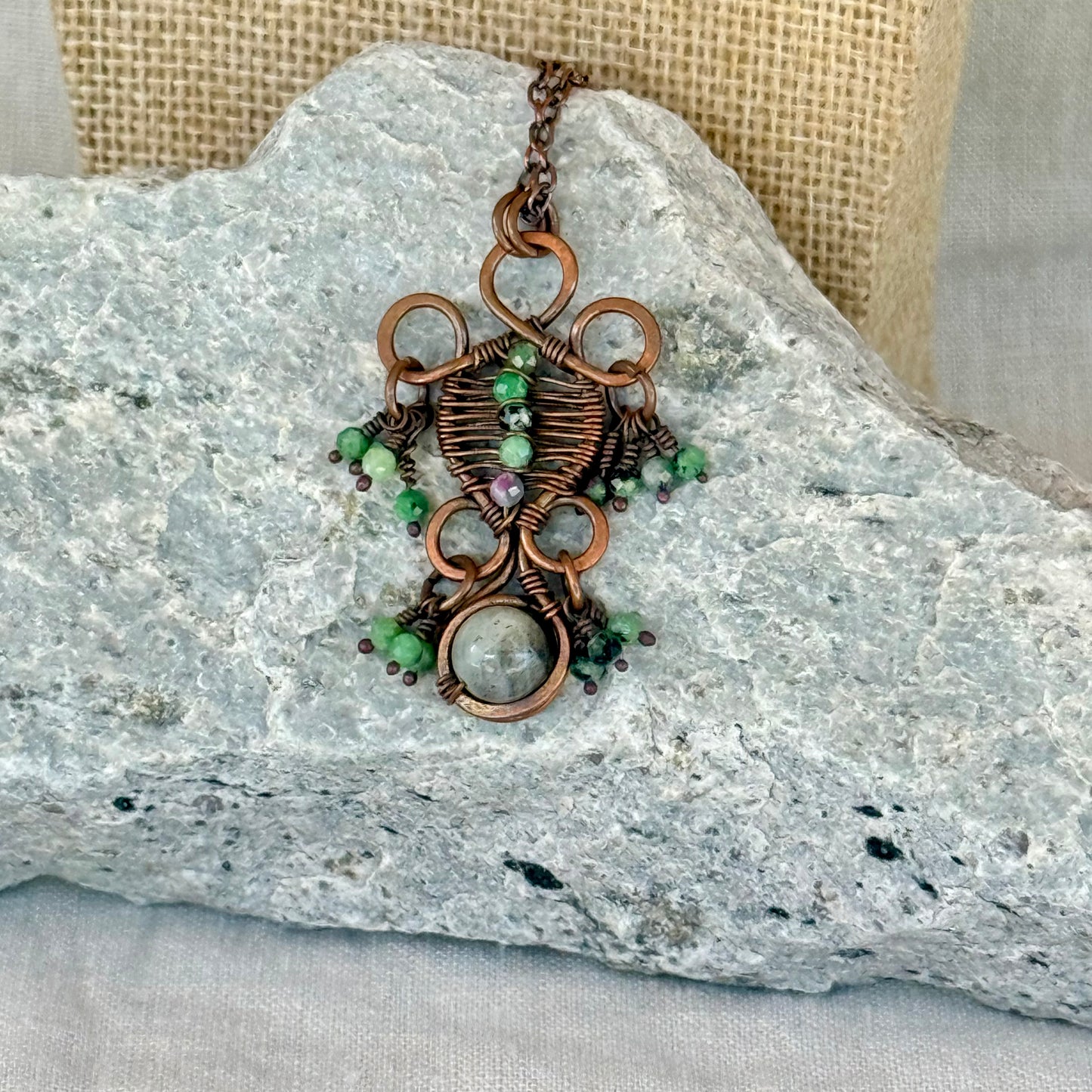 Copper Pendant Necklace with green gemstones on a stone surface with fabric background