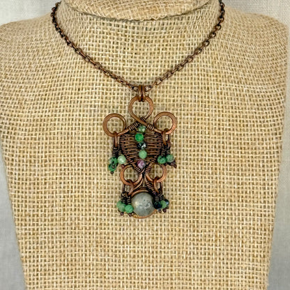 Copper Pendant Necklace with a green gemstones on a textured fabric background
