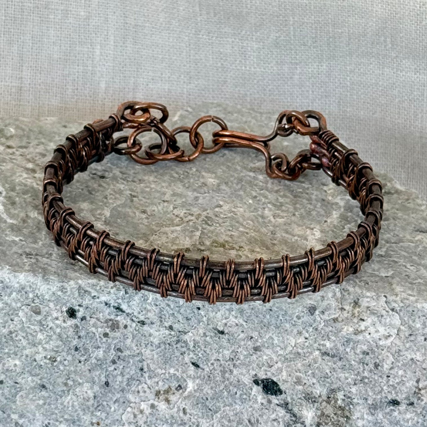 woven copper wire  bracelet on a stone surface with a linen background