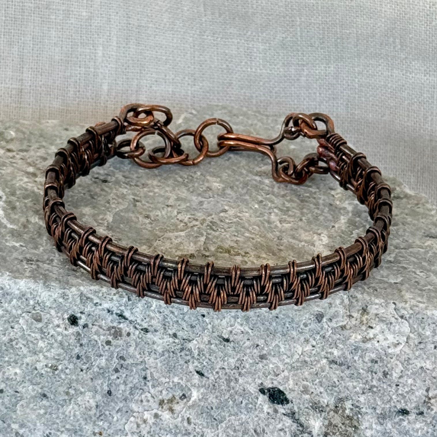 woven copper wire  bracelet on a stone surface with a linen background