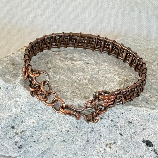woven copper wire  bracelet on a stone surface with a linen background