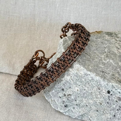 woven copper wire  bracelet on a stone surface with a linen background