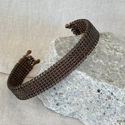 woven copper wire  bracelet on a stone surface with a linen background