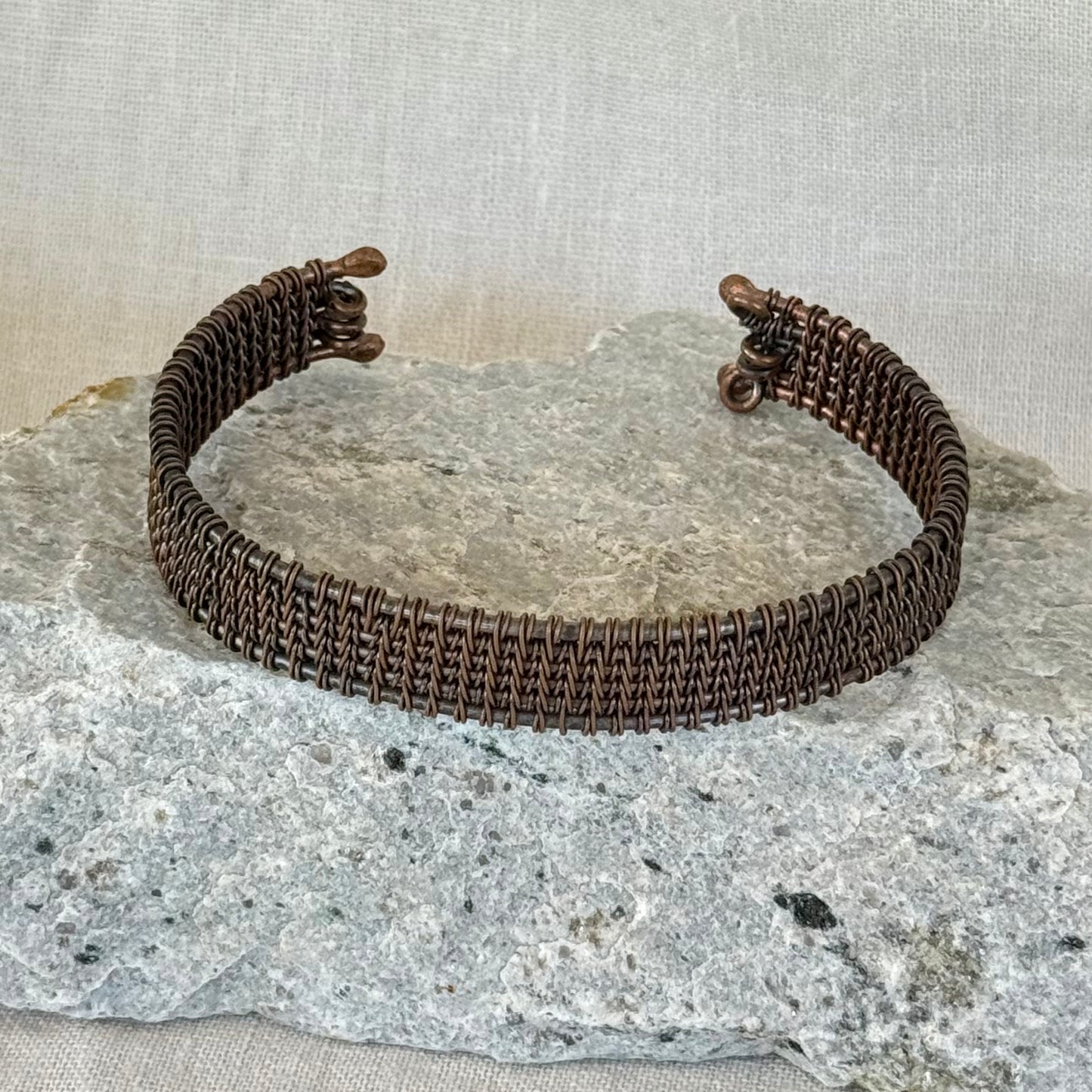 woven copper wire  bracelet on a stone surface with a linen background