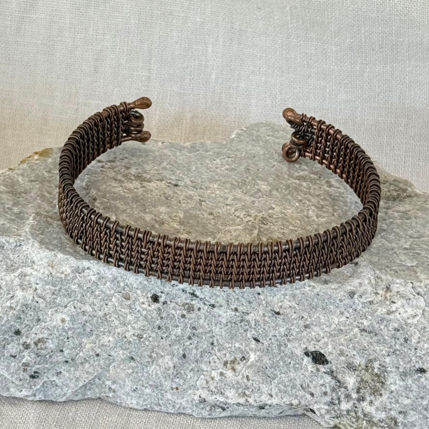 woven copper wire  bracelet on a stone surface with a linen background
