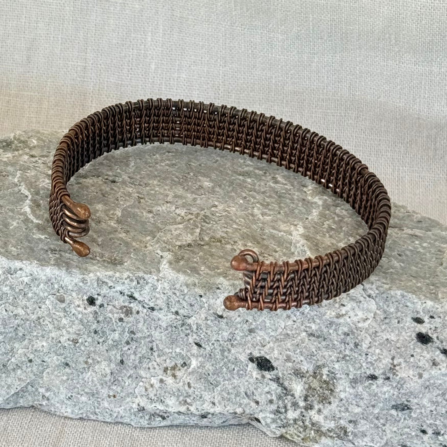 woven copper wire  bracelet on a stone surface with a linen background