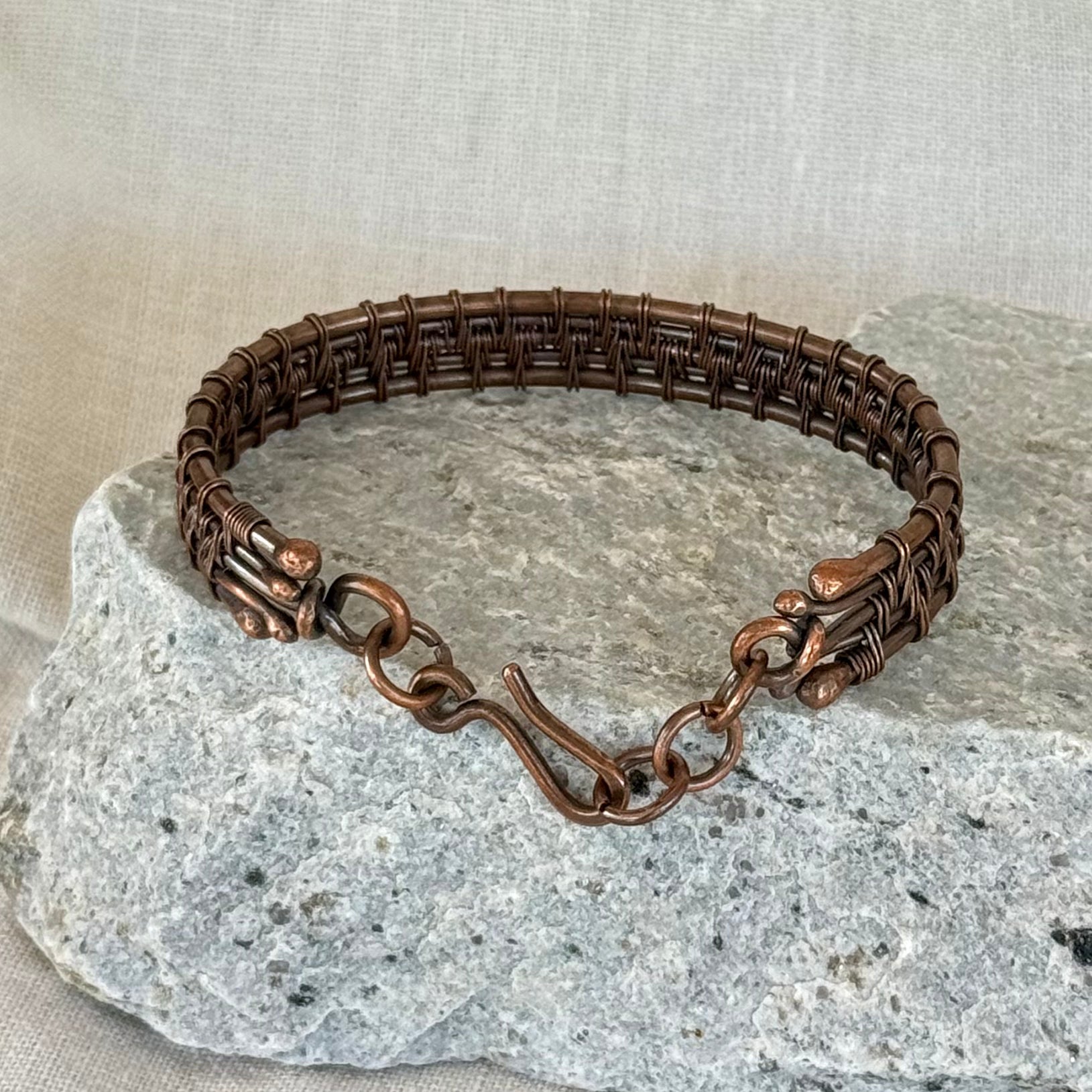 woven copper wire  bracelet on a stone surface with a linen background