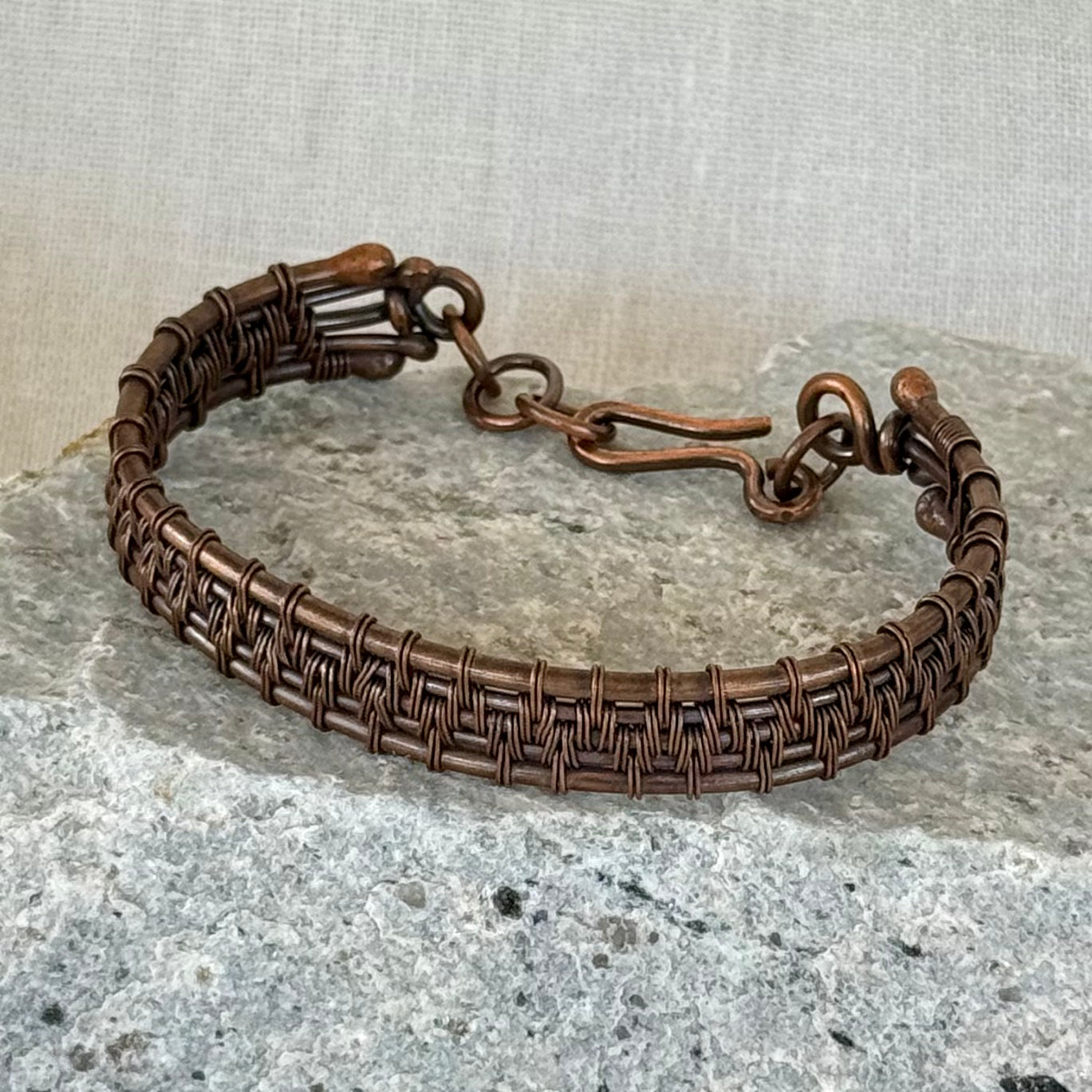 woven copper wire  bracelet on a stone surface with a linen background