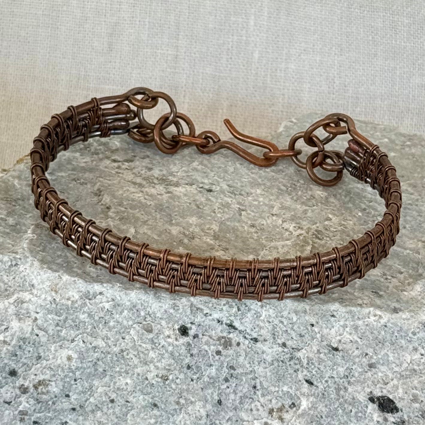 woven copper wire  bracelet on a stone surface with a linen background