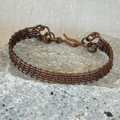woven copper wire  bracelet on a stone surface with a linen background