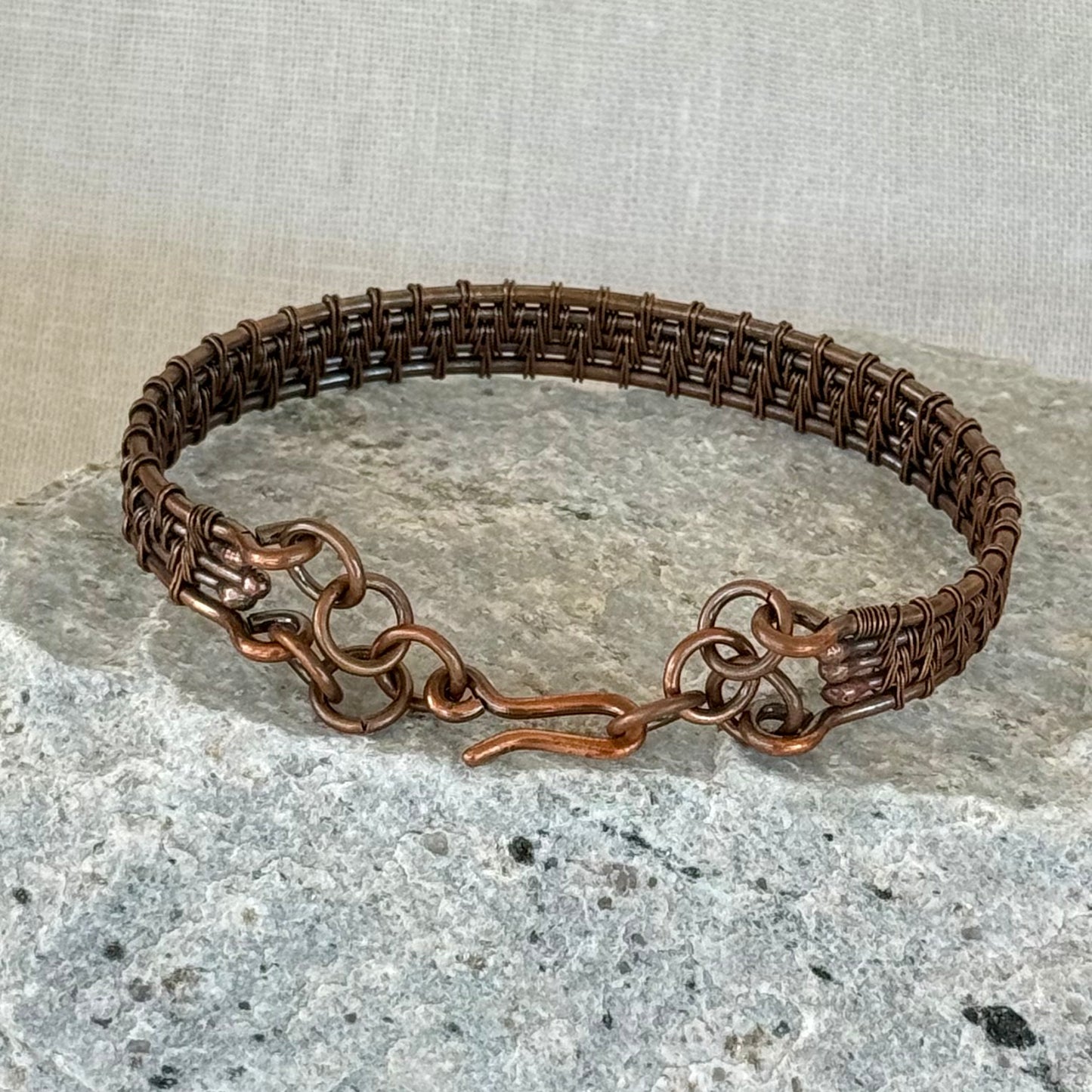 woven copper wire  bracelet on a stone surface with a linen background