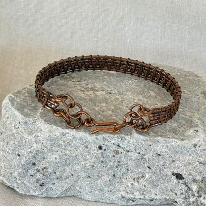 woven copper wire  bracelet on a stone surface with a linen background