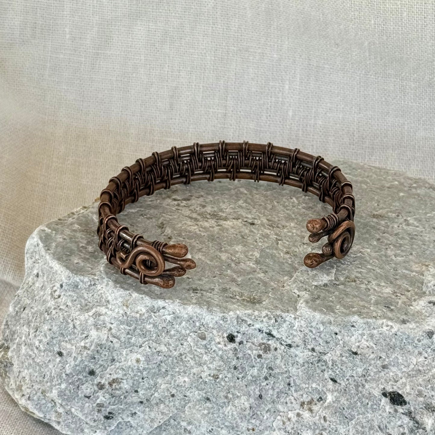woven copper wire  bracelet on a stone surface with a linen background
