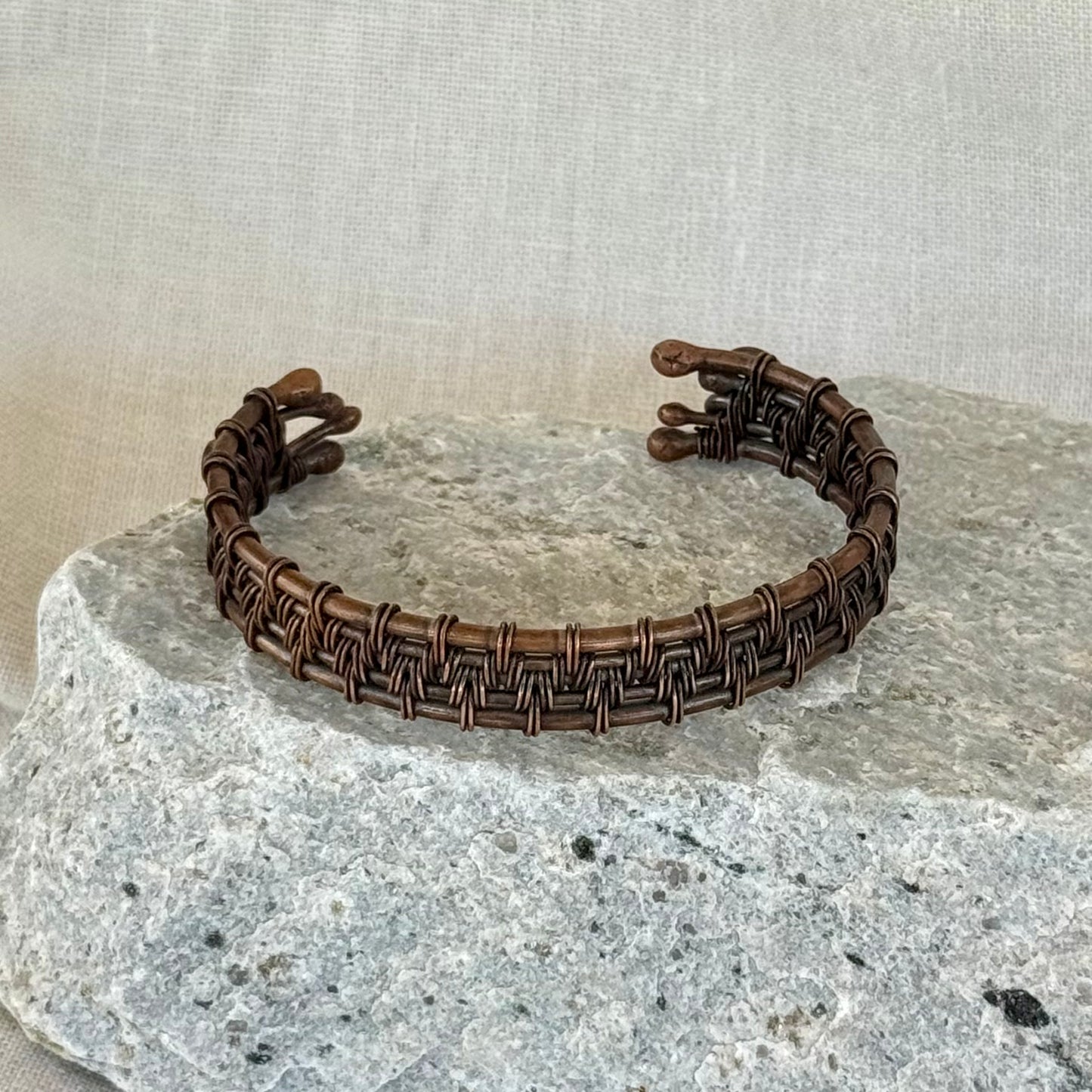 woven copper wire  bracelet on a stone surface with a linen background