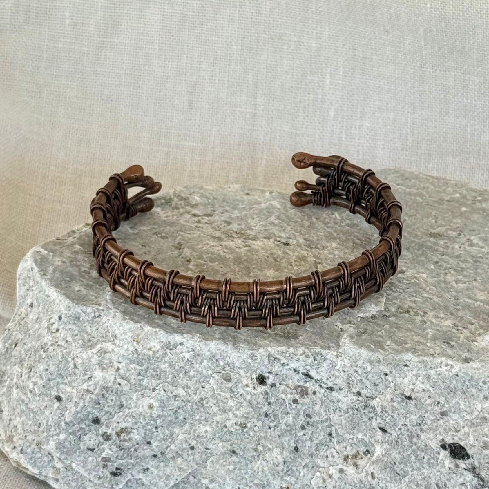 woven copper wire  bracelet on a stone surface with a linen background