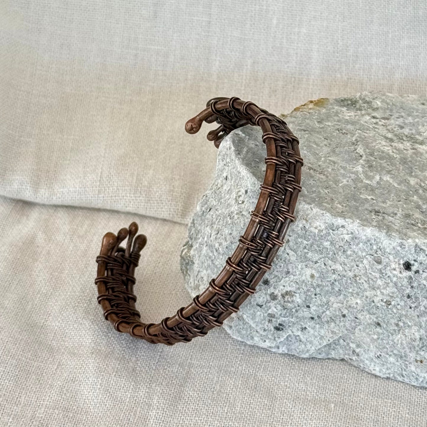 woven copper wire  bracelet on a stone surface with a linen background