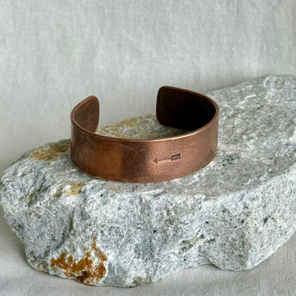 Copper bracelet with stamped arrow on it, on a stone on linen background