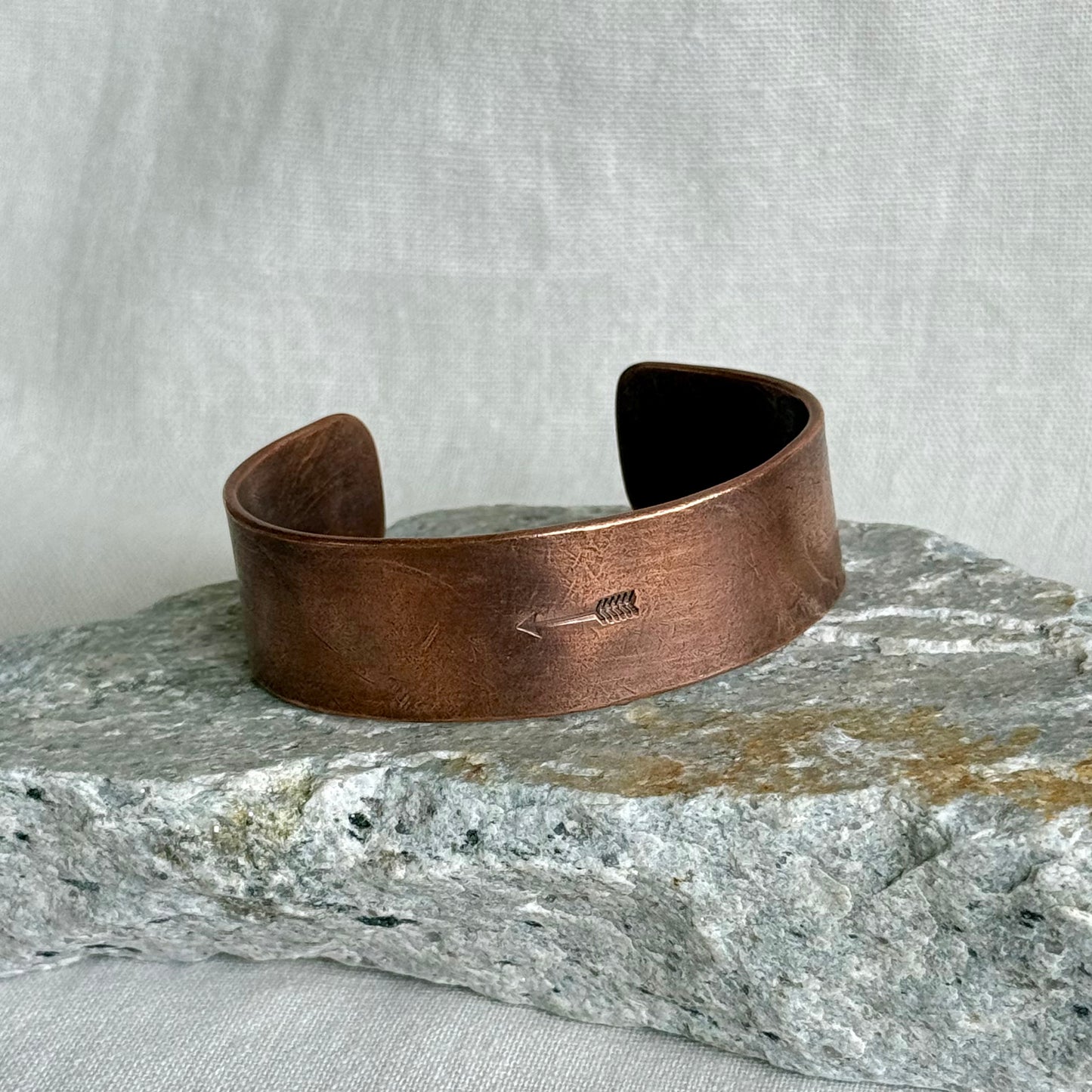 Copper bracelet with stamped arrow on it, on a stone on and linen background