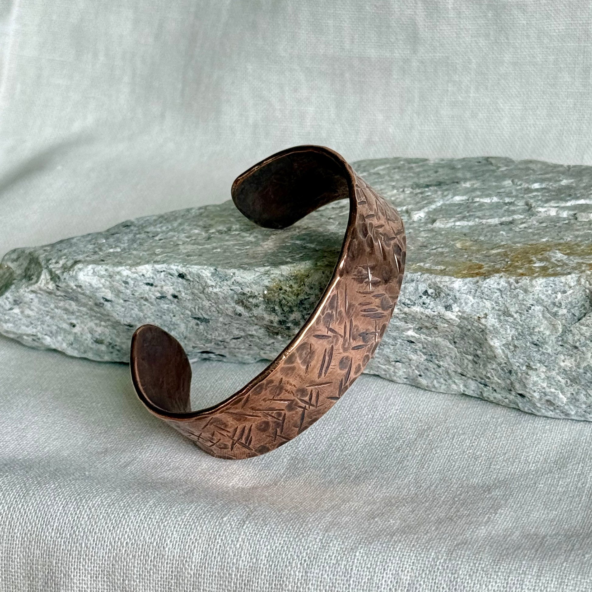 Textured Copper cuff bracelet on a textured surface with a stone background