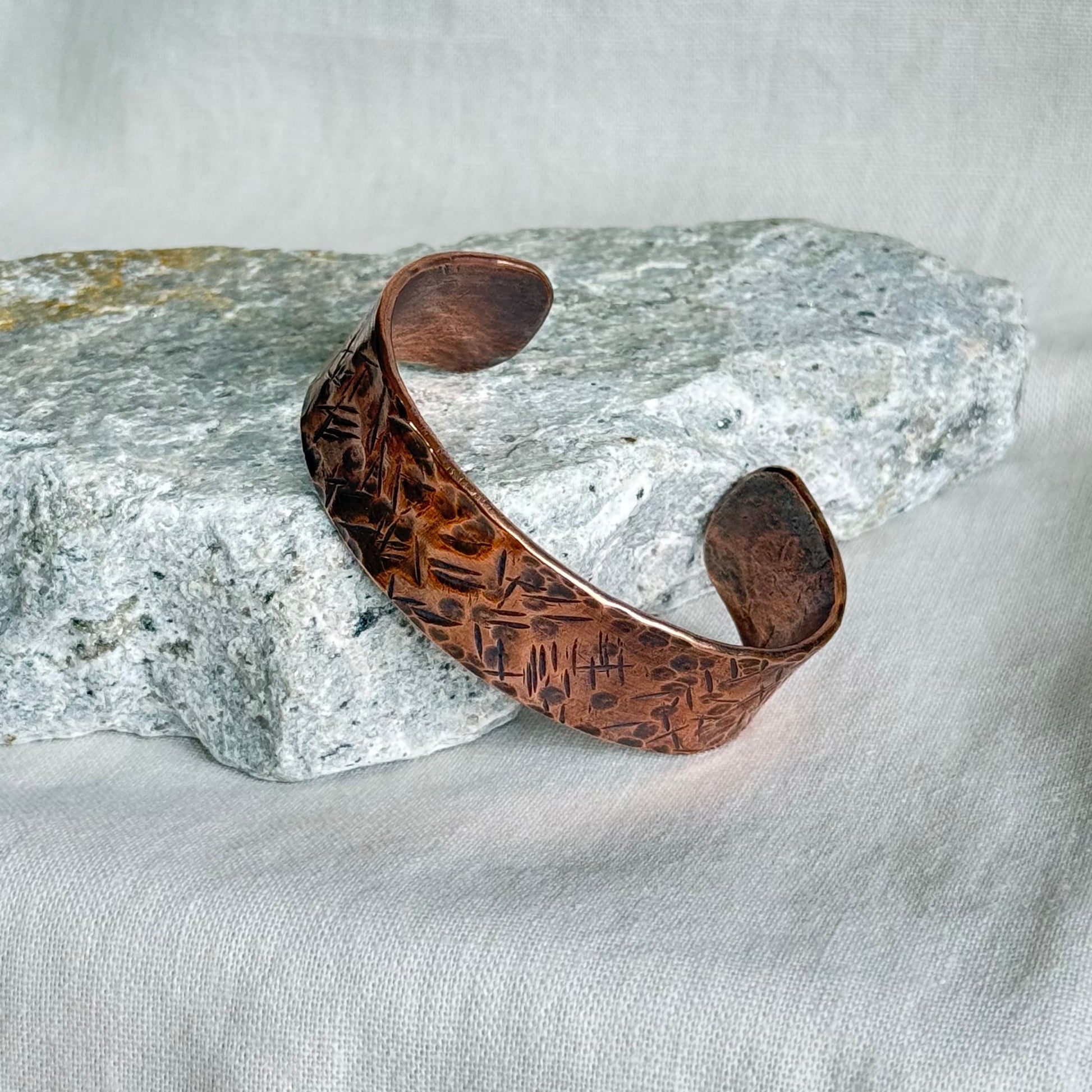Textured Copper cuff bracelet on a textured surface with a stone background
