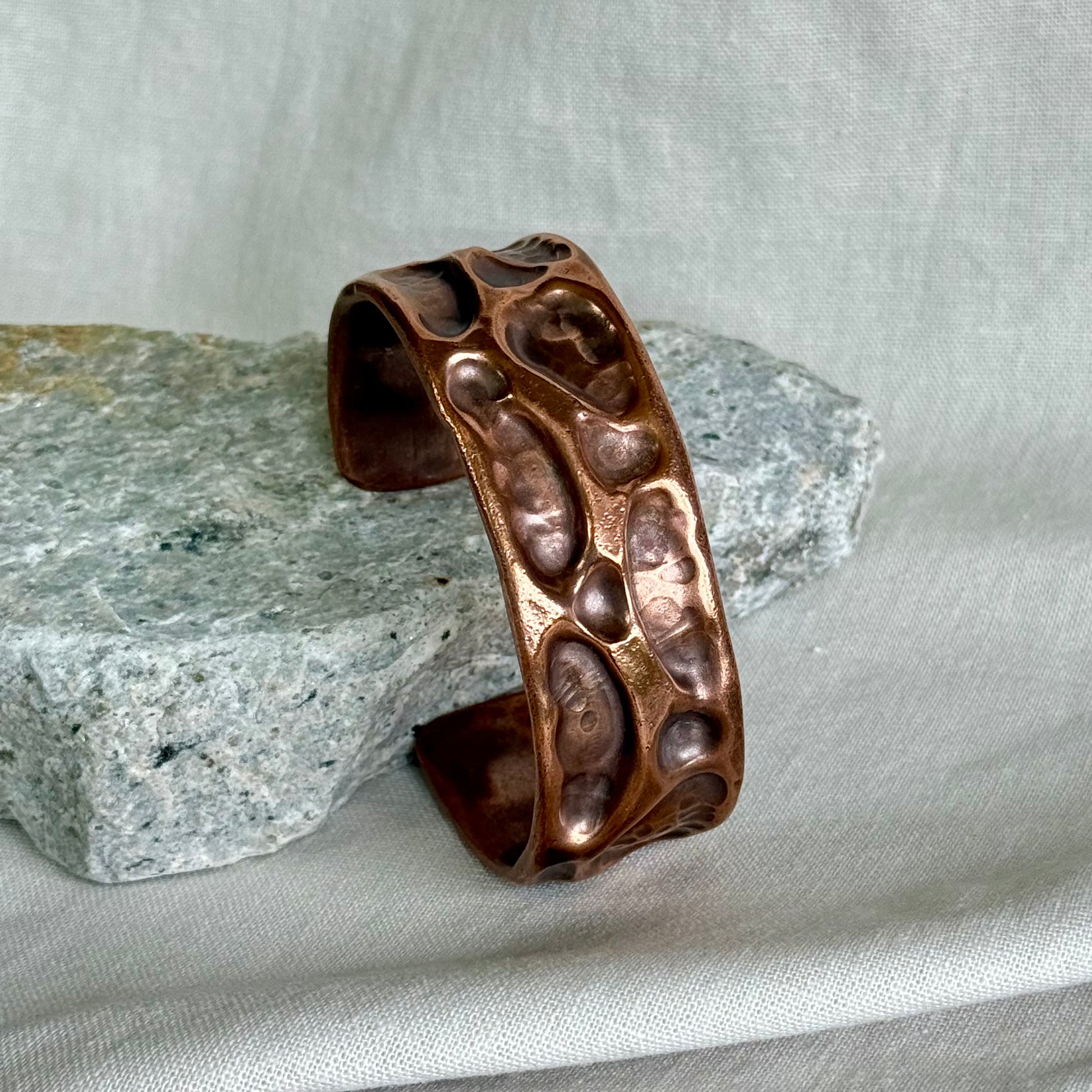 copper cuff with textured surface leaning on a stone with cream background