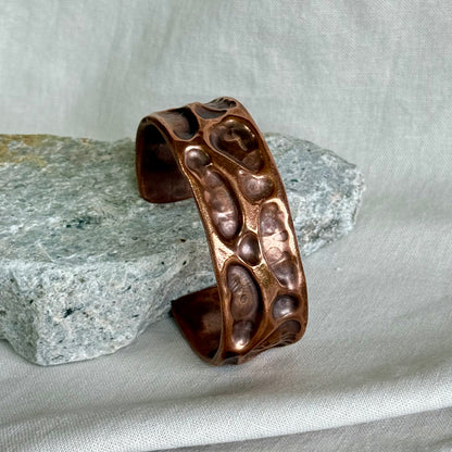 copper cuff with textured surface leaning on a stone with cream background