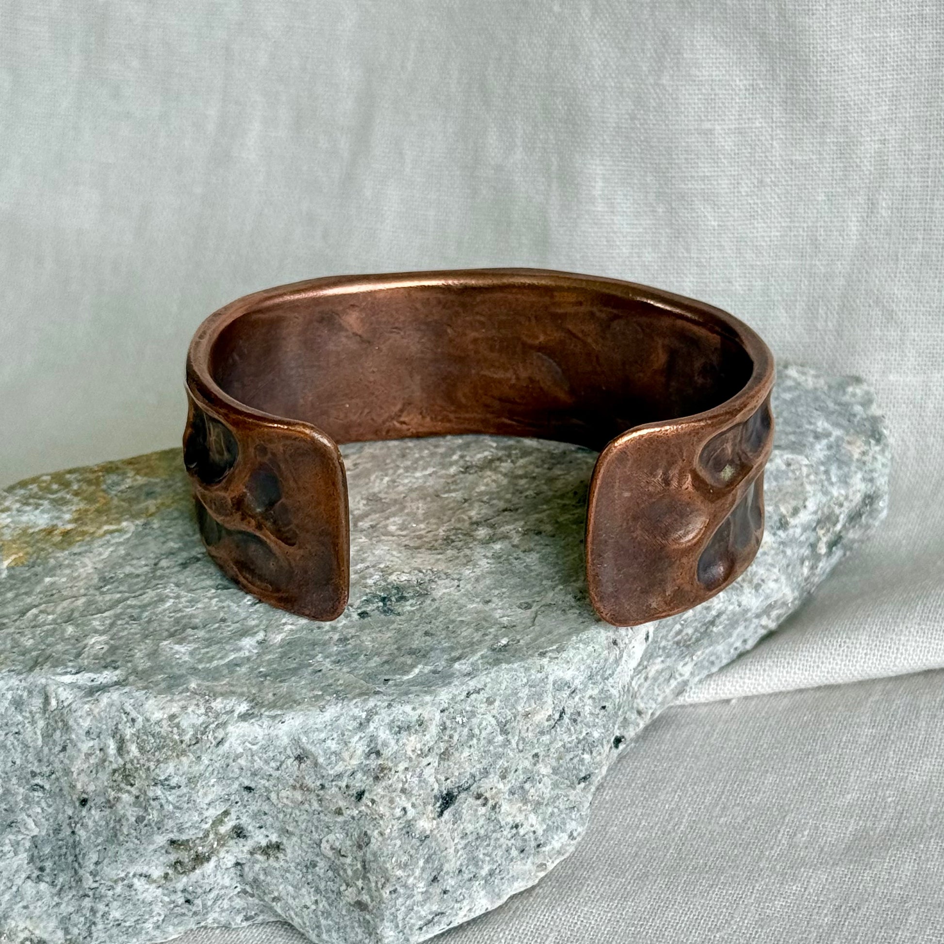 back of a copper cuff with textured surface leaning on a stone with cream background