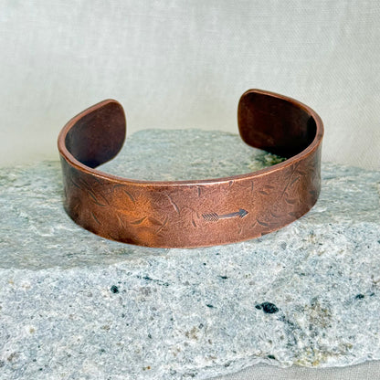 Copper bracelet with stamped arrow on it, on a stone and linen background