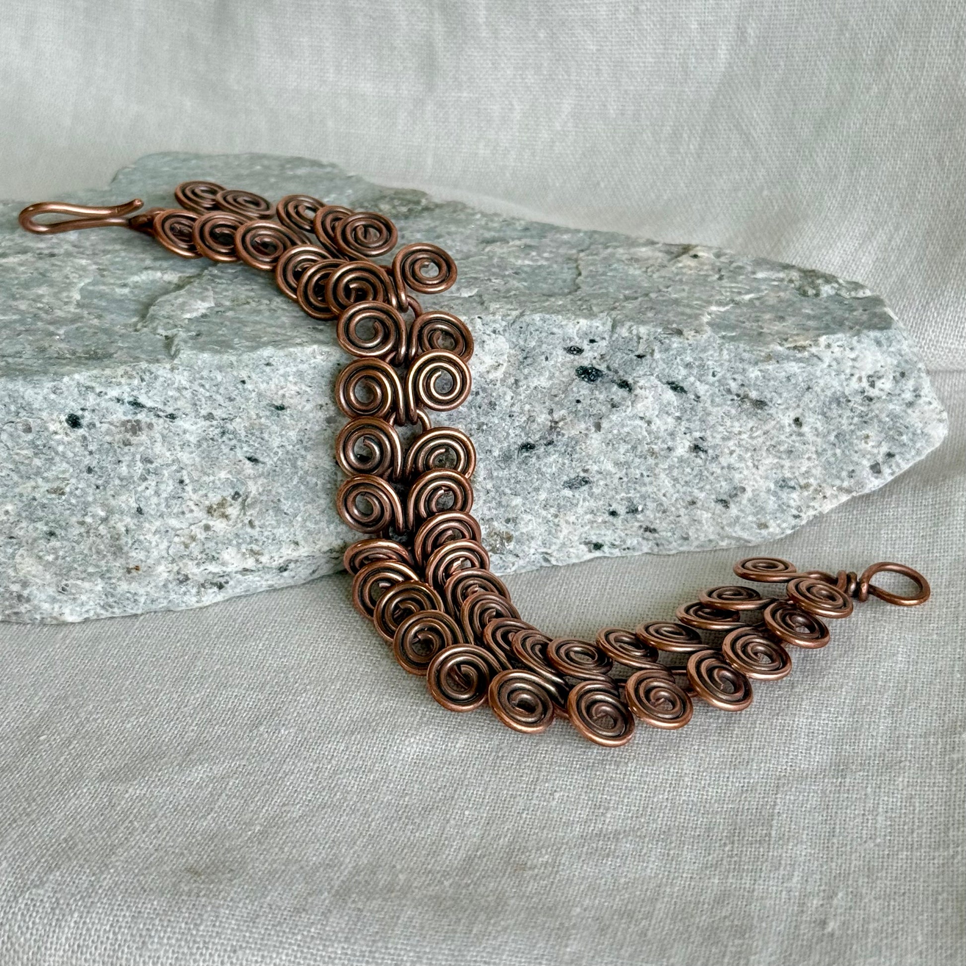 Copper bracelet with intricate spiral design on a stone and fabric background
